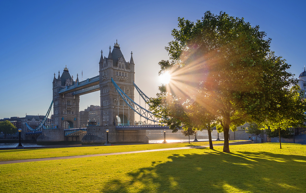 London, Großbritannien – berühmte Tower Bridge bei Sonnenaufgang mit Sonnenlicht, Bäumen, blauem Himmel und grünem Gras