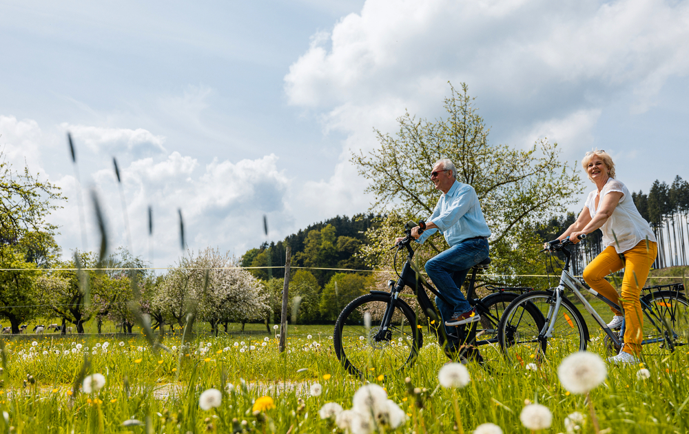 älteres Paar fährt im Frühling mit dem Fahrrad durch eine Wiese