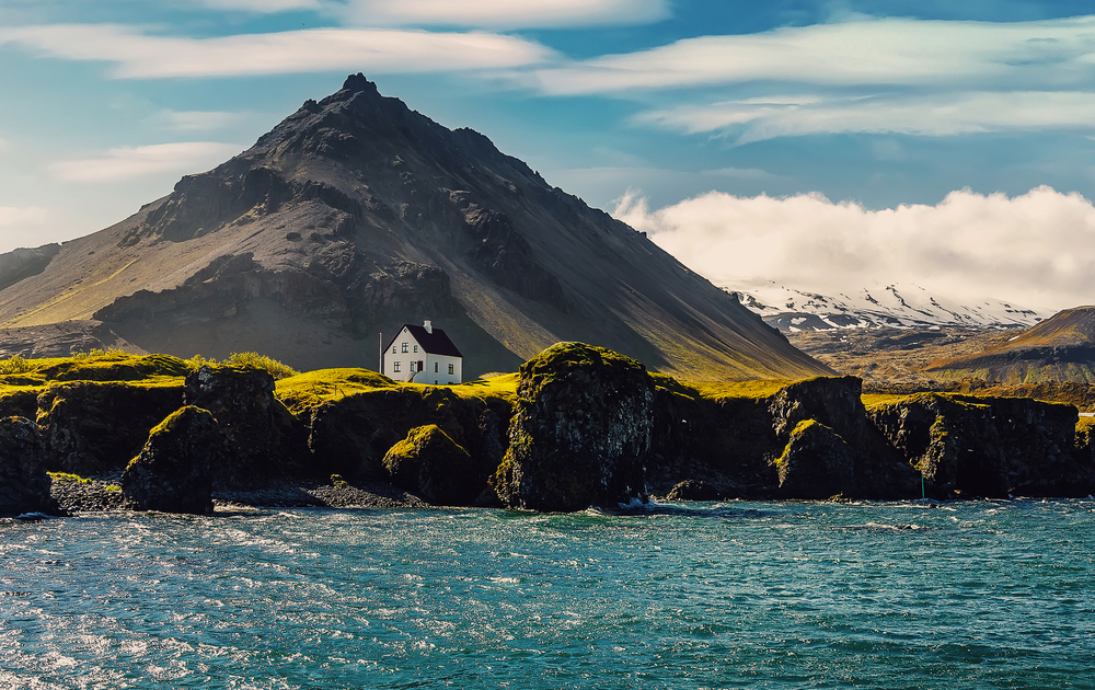Iisländische Landschaft bei Sonnenuntergang mit Häusern vor den Bergen im Dorf Arnarstapi auf der Halbinsel Snafellsnes