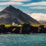 Iisländische Landschaft bei Sonnenuntergang mit Häusern vor den Bergen im Dorf Arnarstapi auf der Halbinsel Snafellsnes