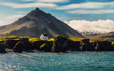 Iisländische Landschaft bei Sonnenuntergang mit Häusern vor den Bergen im Dorf Arnarstapi auf der Halbinsel Snafellsnes