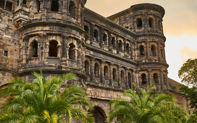 Historisches römisches Gebäude mit Bögen und Palmen im Vordergrund.