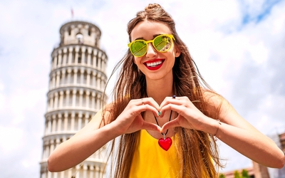 Frau mit Herzhandzeichen vor dem Schiefen Turm von Pisa.