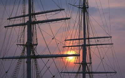 Schiffsmasten bei Sonnenuntergang mit einem orangefarbenen Himmel im Hintergrund.