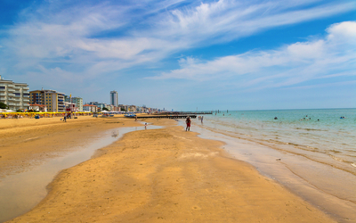 Strand mit Gebäuden im Hintergrund, klarem Himmel und wenigen Menschen im Wasser.