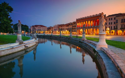 Fluss mit Brücke und beleuchteten Gebäuden bei Dämmerung in einer europäischen Stadt.