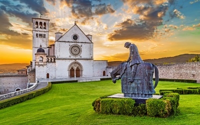 Kirche in Assisi mit Reiterstatue und Sonnenuntergang im Hintergrund.