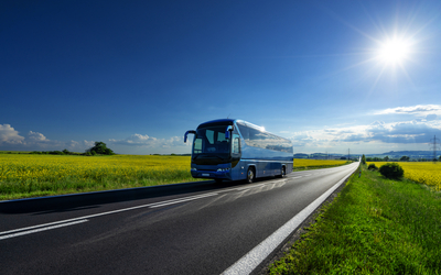 Reisebus auf Landstraße bei sonnigem Wetter.