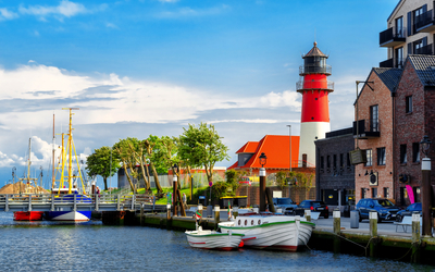 Küstenstadt mit Leuchtturm, Segelbooten und roten Backsteinhäusern am Wasser.