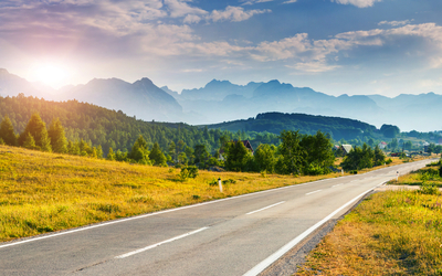 Landschaft mit Straße, Wiese und Bergen im Sonnenuntergang.