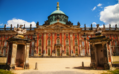 Barockes Schloss mit Kuppel, durch ein Tor gesehen, blauer Himmel im Hintergrund.