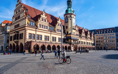 Historisches Gebäude mit Turm auf großem, belebtem Platz bei blauem Himmel.
