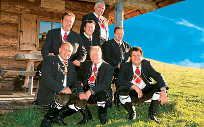 Mehrere Männer in traditioneller Tracht vor einer Holzhütte.