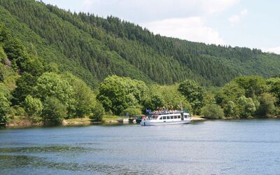 Schiff fährt auf See umgeben von bewaldeten Hügeln der Rurtalsperre in NRW.