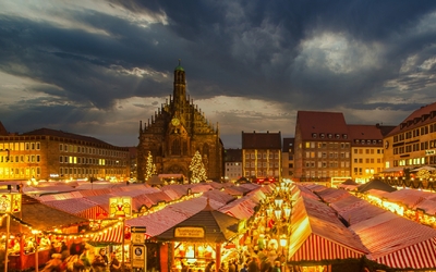 Abendlicher Weihnachtsmarkt mit beleuchteten Ständen und gotischer Kirche im Hintergrund.