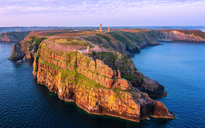 Klippen mit Leuchtturm an der Küste bei Sonnenuntergang.