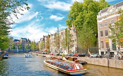 Boot fährt durch einen Kanal in Amsterdam, gesäumt von Bäumen und alten Gebäuden.