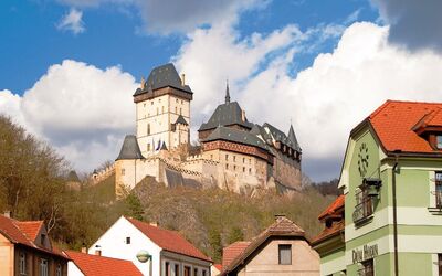 Burg auf einem Hügel mit umliegenden Gebäuden und bewölktem Himmel.