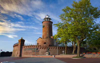 Backstein-Leuchtturm mit Baum davor unter blauem Himmel am Abend.