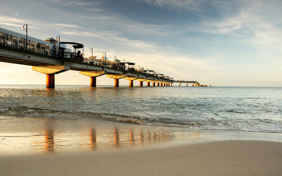 Steg über dem Meer bei Sonnenuntergang mit welligem Wasser und Sandstrand