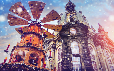 Weihnachtspyramide vor historischer Kirche mit Schneefall im Hintergrund.