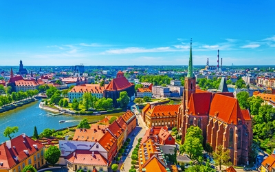 Stadtansicht mit Fluss, Kirchen und roten Dächern unter blauem Himmel.