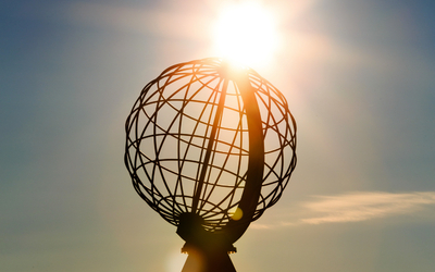 Sonnenuntergang am Nordkap mit Touristen und Weltkugel-Skulptur.