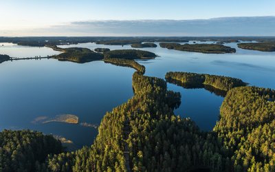 Luftaufnahme von Seenlandschaft mit bewaldeten Inseln unter blauem Himmel.