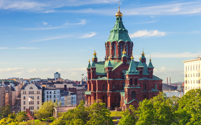 Orthodoxe Kathedrale in Helsinki, von Bäumen umgeben, unter blauem Himmel.