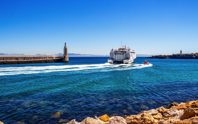 Fähre verlässt Hafen auf blauem Meer unter klarem Himmel.