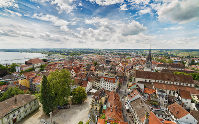 Panoramablick auf eine historische Stadt mit Kirche und See im Hintergrund.