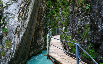 Holzsteg schlängelt sich entlang einer engen Schlucht mit türkisfarbenem Fluss.