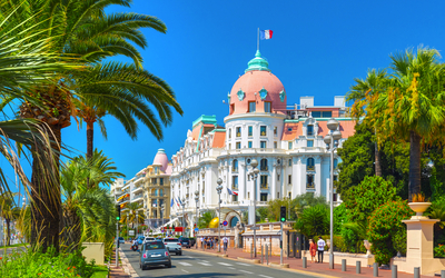 Boulevard in Nizza mit Hotel und Palmen im Vordergrund.