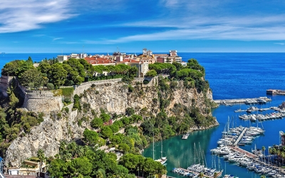 Küstenpanorama mit Yachthafen und historischem Gebäude auf einem Hügel.
