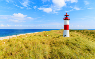 Leuchtturm in einer Dünenlandschaft am Meer bei sonnigem Wetter.