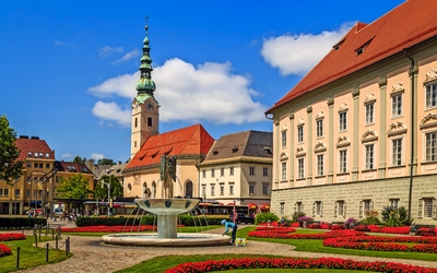 Stadtplatz mit Brunnen, Blumenbeeten und historischem Gebäude bei sonnigem Wetter