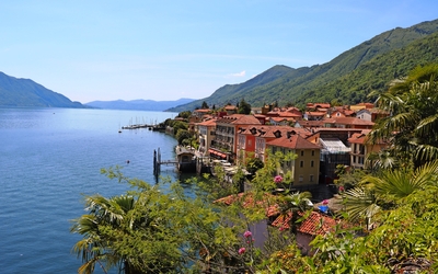 Küstenstadt mit bunten Häusern, umgeben von Bergen und einem See unter blauem Himmel.