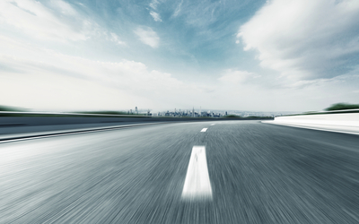 Leere Autobahn mit Blick auf entfernte Stadt bei blauem Himmel.