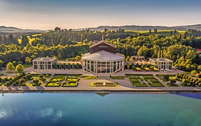 Luftaufnahme eines Theaters am Wasser mit Gartenanlage im Vordergrund.