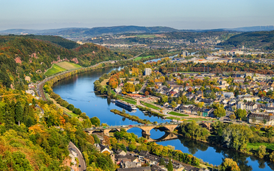 Landschaft mit Fluss, Stadtpanorama und Brücke bei sonnigem Wetter.
