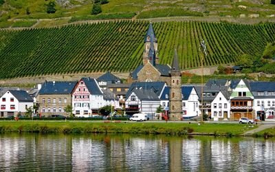 Ortsansicht von Müden an der Mosel mit Kirche und Weinbergen im Hintergrund.