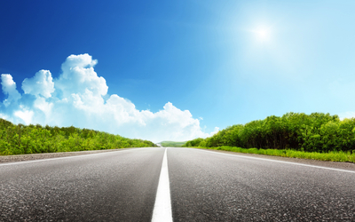 Längere Straße unter blauem Himmel mit weißen Wolken und grünem Wald.