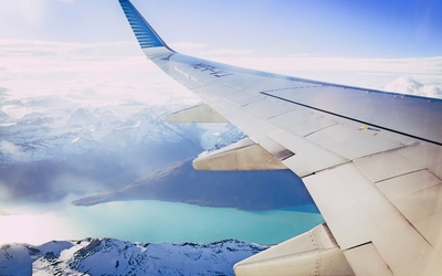 Blick aus dem Flugzeugfenster auf schneebedeckte Berge und einen See.