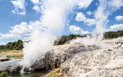 Geysir mit aufsteigendem Dampf in einer felsigen Landschaft bei blauem Himmel.