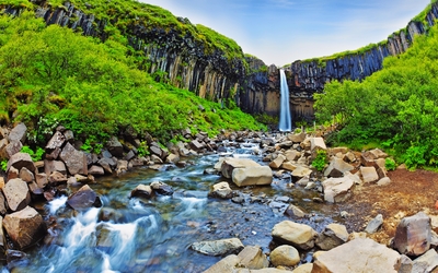 Wasserfall in einer grün bewachsenen Schlucht mit Basaltsäulen.