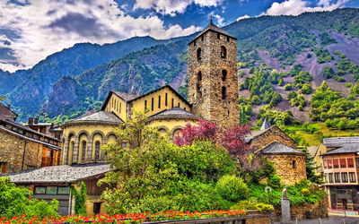 Eine alte Steinkirche vor bewaldeten Bergen und blühenden Gärten.