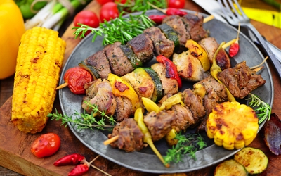 Grillspieße mit Fleisch und Gemüse, serviert mit Maiskolben und frischen Kräutern.