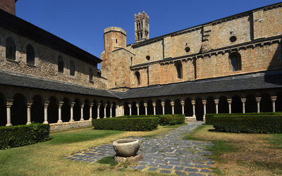 Innenhof eines Klosters mit begrüntem Garten und romanischer Architektur.