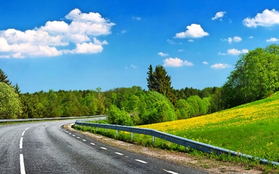 Landstraße mit Kurve durch grüne Landschaft unter blauem Himmel.