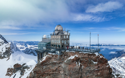 Observatorium auf schneebedecktem Berggipfel unter blauem Himmel.
